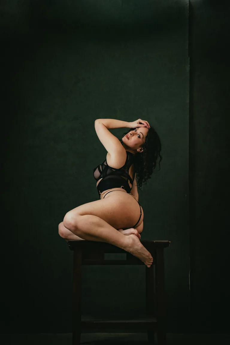 Studio boudoir portrait in dark lingerie on an antique chair, deep green backdrop