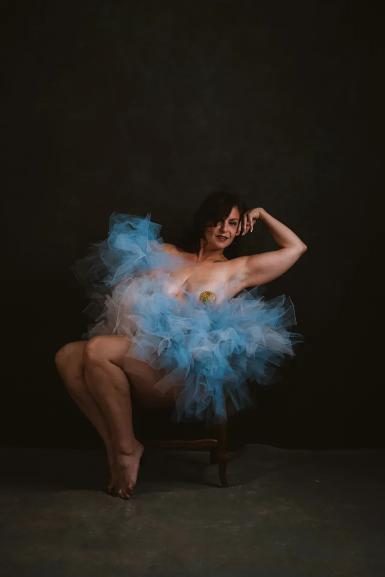 Conceptual studio portrait with a cloud of blue tulle against a green backdrop, arm raised — joyful editorial